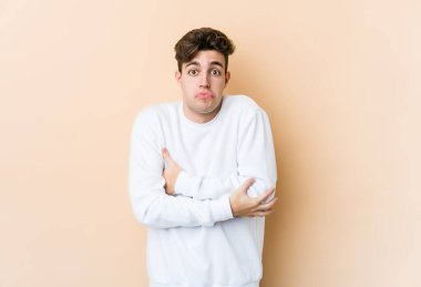 Beyazlı genç adam bej arka planda izole edilmiş omuzlarını silkeliyor ve gözleri açık..