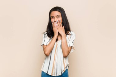 Genç sevimli Çinli genç sarışın kadın pembe arka planda palto giyiyor. Bir şeylere gülüyor, elleriyle ağzını kapatıyor..