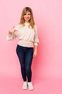 Pembe arka planda duran genç sarışın kadın. Elle bir tişört fotokopi alanını işaret ediyor. Gururlu ve kendinden emin.