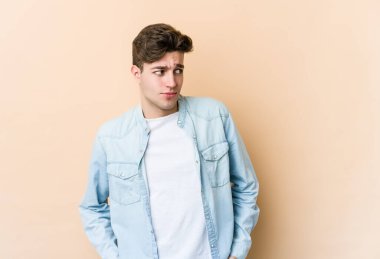 Kafkasyalı genç adam bej arka planda izole, kafası karışmış, şüpheli ve güvensiz hissediyor..