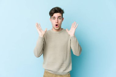 Kafkasyalı genç adam mavi arka planda izole edildi. Şaşırdı ve şok oldu..