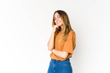 Beyaz arka planda izole edilmiş genç beyaz kadın mutlu ve kendinden emin gülümsüyor, elleriyle çenesine dokunuyor..