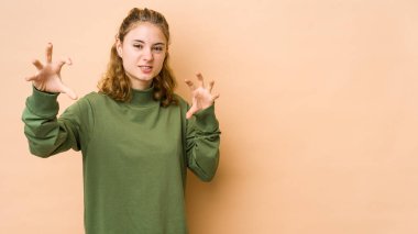 Bej arka planda izole edilmiş genç beyaz kadın gergin elleriyle çığlık atıyor..