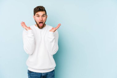 Kafkasyalı genç adam mavi arka planda izole edildi. Şaşırdı ve şok oldu..