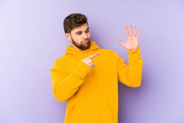 Mor arka planda izole edilmiş genç adam gülümseyerek beş numarayı parmaklarıyla gösteriyor..