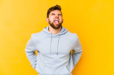 Sarı arka planda izole edilmiş beyaz bir genç. Komik ve dost canlısı bir dil uzatıyor..