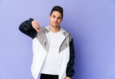 Mor arka planda izole edilmiş genç beyaz bir adam hoş olmayan bir jest yapıyor, başparmakları aşağıda. Anlaşmazlık konsepti.