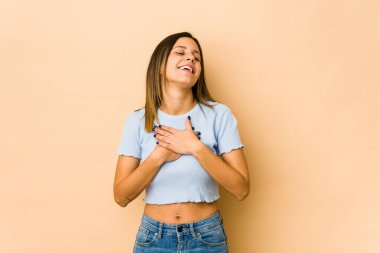 Bej arka planda izole edilmiş genç bir kadın, dostane bir ifadeye sahip, avuçlarını göğsüne bastırıyor. Aşk konsepti.