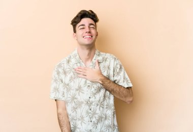 Beyaz tenli genç adam bej arka planda izole edilmiş. Kahkahalar atıyor..