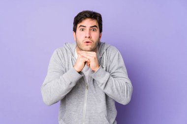 Mor arka planda izole edilmiş genç bir adam şans için dua ediyor, şaşırmış ve ağzı açık bir şekilde önüne bakıyor..