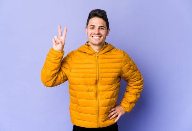 Mor arka planda izole edilmiş genç beyaz adam iki numarayı parmaklarıyla gösteriyor..