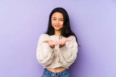 Mor arka planda izole edilmiş genç Çinli bir kadın avuçlarıyla bir şey tutuyor ve kameraya sunuyor..