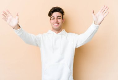 Beyazlı genç bir adam bej arka planda izole edilmiş bir şekilde zaferi veya başarıyı kutluyor. Şaşırmış ve şok olmuş..