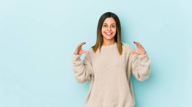 Mavi arka planda izole edilmiş genç bir kadın elinde avuç içi bir şeyle kameraya sunuyor..