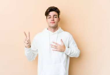 Beyaz tenli genç adam bej arka planda izole edilmiş yemin ediyor, elini göğsüne koyuyor..