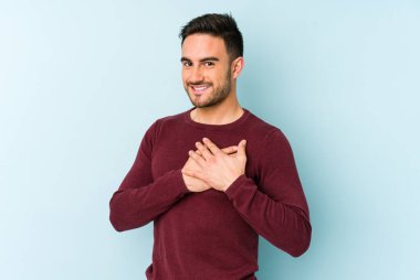 Mavi arka planda izole edilmiş beyaz bir genç, dost bir ifadeye sahip, avuçlarını göğsüne bastırıyor. Aşk konsepti.