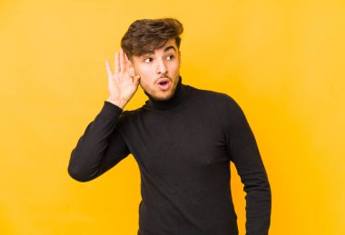 Sarı arka planda yaşayan genç bir Arap adam bir dedikoduyu dinlemeye çalışıyor..