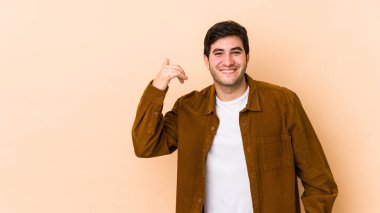 Bej arka planda izole edilmiş genç bir adam bir şeye gülüyor, elleriyle ağzını kapatıyor..