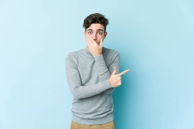 Mavi arka planda izole edilmiş genç beyaz adam yan tarafı işaret ediyor.