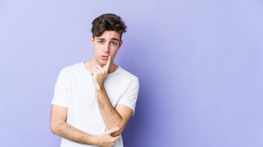 Mor arka planda izole edilmiş genç beyaz adam şüpheli ve şüpheci bir ifadeyle yana bakıyor..