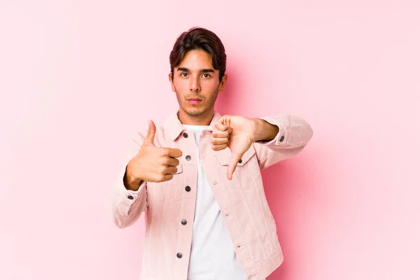 年轻的高加索男子装扮成粉红的背景孤立地展示大拇指向上和向下 难以选择的概念 — 图库照片
