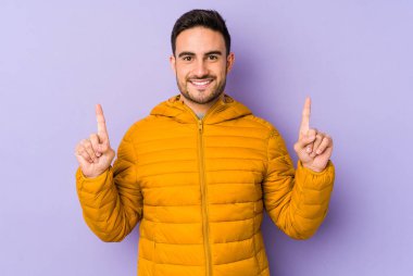 Mor arka planda izole genç beyaz adam iki ön parmağı da boş bir alan gösteriyor..