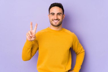 Mor arka planda izole edilmiş genç beyaz adam neşeli ve kaygısız parmakları olan bir barış sembolü gösteriyor..