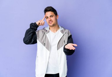 Mor arka planda izole edilmiş genç beyaz adam elinde bir ürün tutuyor..