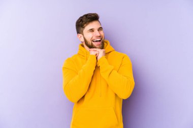 Mor arka planda izole genç adam ellerini çenesinin altında tutuyor, mutlu bir şekilde yan tarafa bakıyor..