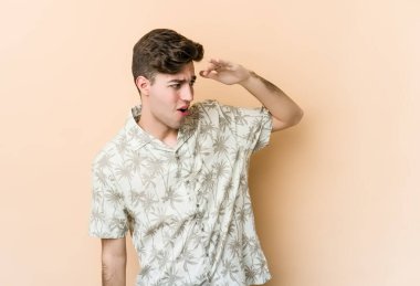 Beyazlı genç bir adam bej arka planda izole edilmiş, uzaklara bakıyor ve elini alnına koyuyor..