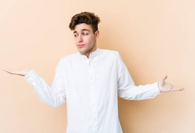 Kafkasyalı genç adam bej arka planda izole edilmiş. Kafası karışmış ve omuz silkiyor. Kopya alanını tutmak için..