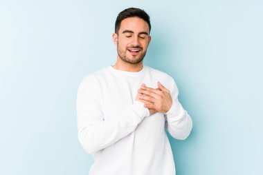 Mavi arka planda izole edilmiş beyaz bir genç, dost bir ifadeye sahip, avuçlarını göğsüne bastırıyor. Aşk konsepti.