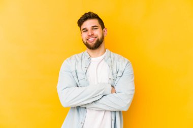 Sarı arka planda izole edilmiş genç beyaz adam kendini güvende hissediyor, kararlılıkla kollarını kavuşturuyor..