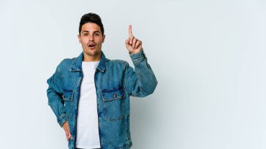 Beyaz arka planda izole edilmiş genç beyaz adam ağzı açık bir şekilde üst tarafı işaret ediyor..