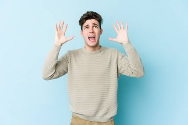 Kafkasyalı genç adam mavi arka planda izole edilmiş gökyüzüne haykırıyor, yukarı bakıyor, hayal kırıklığına uğramış..