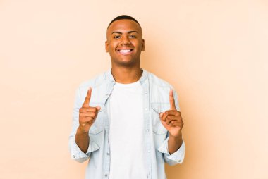 Bej arka planda izole edilmiş genç latin adam iki ön parmağı da boş bir alan gösteriyor..