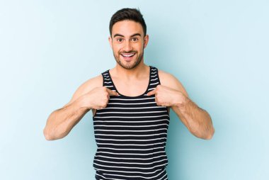 Mavi arka planda izole edilmiş genç beyaz adam parmağını göstererek şaşırdı, geniş bir gülümsemeyle..