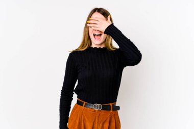 Beyaz arka planda soyutlanmış beyaz tenli genç bir kadın elleriyle gözlerini kapatıyor, geniş bir gülümsemeyle bir sürpriz bekliyor..