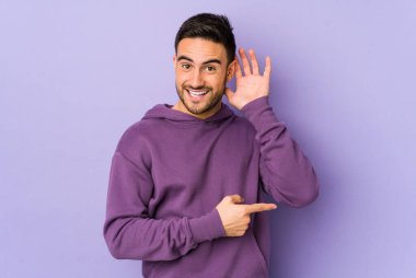 Mor arka planda izole edilmiş genç beyaz bir adam bir dedikoduyu dinlemeye çalışıyor..