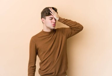 Beyaz tenli genç adam bej arka planda izole edilmiş bir şekilde bir şey unutuyor. Alnına avuç içi ve kapalı gözlerle vuruyor..