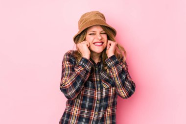 Şapka takan genç beyaz kadın kulaklarını elleriyle kapatıyor..