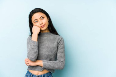 Mavi bir arka planda izole edilmiş genç Çinli kadın üzgün ve düşünceli, fotokopi alanına bakıyor..