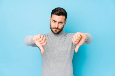 Mavi arka planda genç, beyaz bir adam izole edilmiş, baş parmağını aşağı gösteren ve hoşlanmadığını ifade eden..