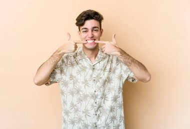 Beyazların arka planında izole edilmiş genç beyaz adam gülümsüyor, parmaklarını ağzına doğrultuyor..