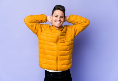 Mor arka planda izole olmuş genç beyaz bir adam kendini güvende hissediyor, elleri başının arkasında..