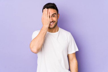 Mor arka planda izole edilmiş genç beyaz adam yüzünün yarısını palmiye ile kaplayarak eğleniyor..