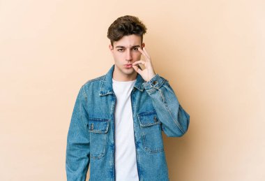 Beyazlı genç bir adam bej arka planda izole edilmiş ve parmakları dudaklarında bir sır saklıyor..