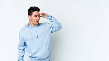 Beyaz arka planda izole edilmiş genç beyaz bir adam uzaklara bakıyor ve elini alnına koyuyor..