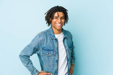 Genç siyah adam kot ceket giyiyor. Kendine güveniyor. Ellerini kalçasından ayırmıyor..