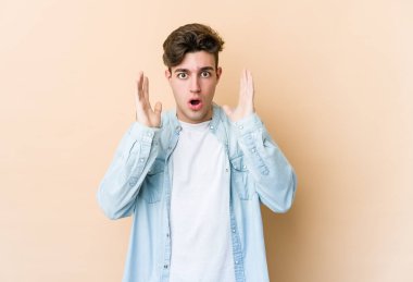 Beyazlı genç bir adam bej arka planda izole edilmiş. Şaşırmış ve şok olmuş..